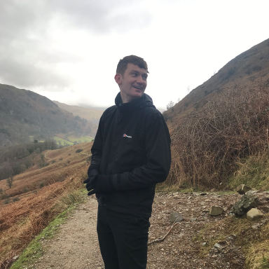 Kieran stands wearing all black with views of mountains in the background